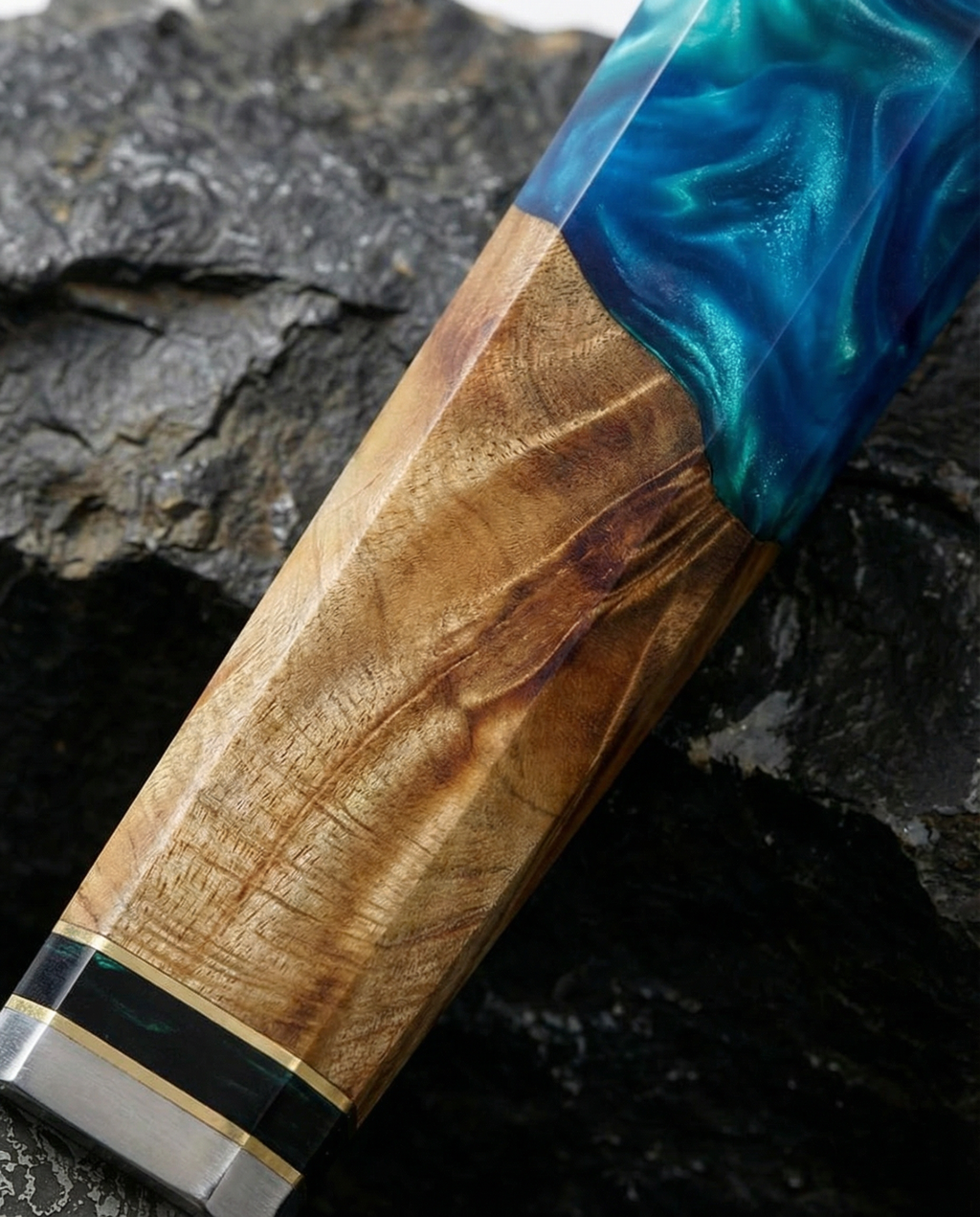 Gros plan sur le manche d’un couteau japonais en bois naturel et résine bleue marbrée, posé sur pierre sombre texturée.