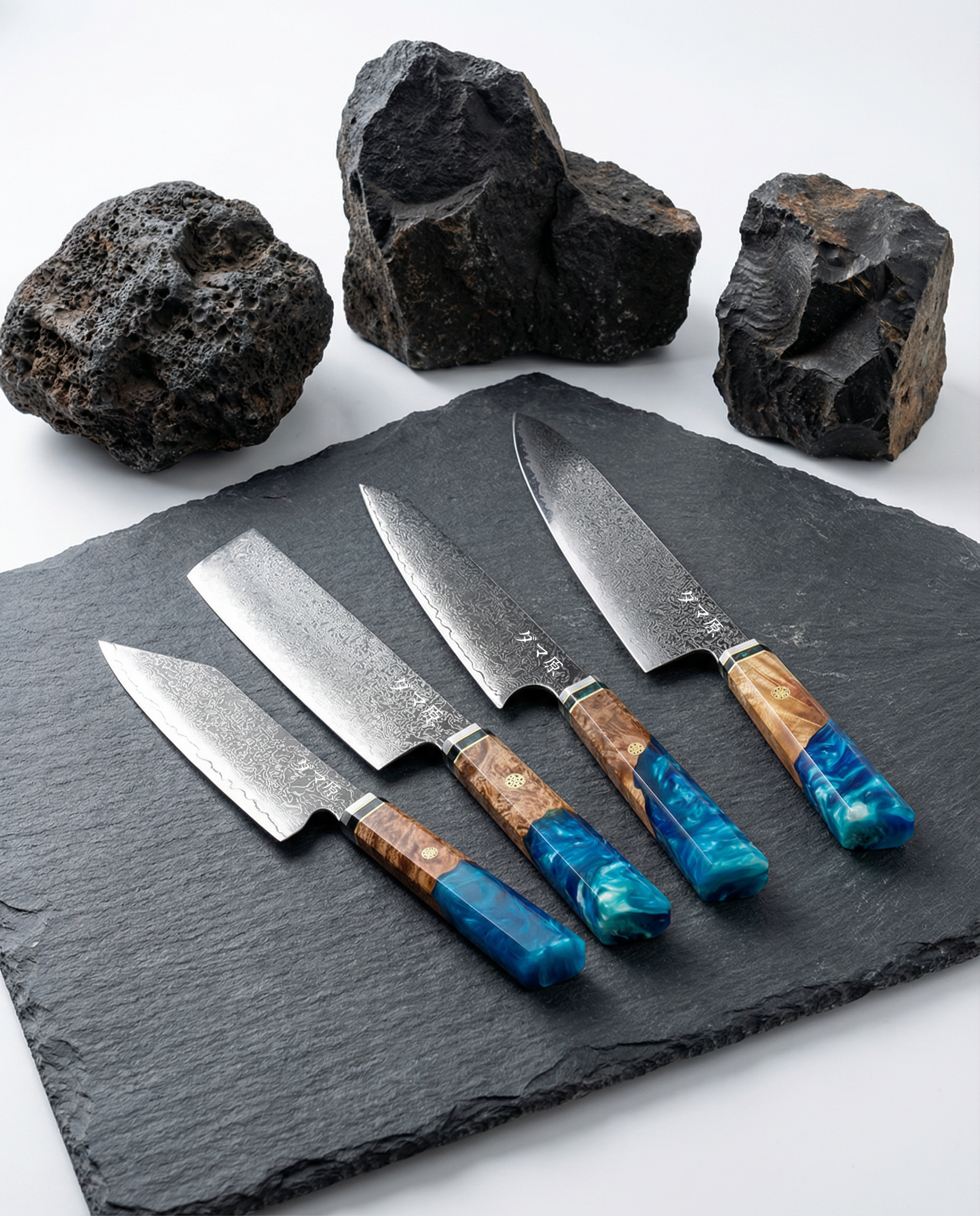 Quatre couteaux japonais en acier damassé sur ardoise noire, manches en bois et résine bleue, pierres volcaniques en décor.