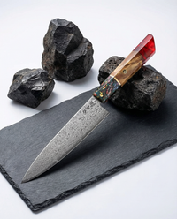 Couteau Petty japonais en acier damassé, manche bois et résine rouge, posé sur ardoise noire avec pierres.