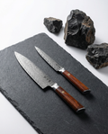 Set de 2 couteaux japonais en acier damassé avec manches bois naturel, posés sur plaque d’ardoise noire.