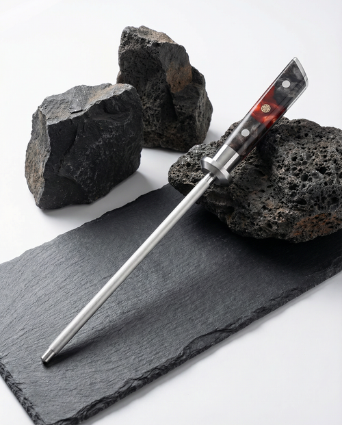 Fusil d’aiguisage professionnel avec manche résine noir et ambre, tige acier lisse, présenté sur ardoise avec pierres volcaniques.