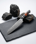 Couteau japonais kiritsuke en acier damas, lame large à pointe angulaire, manche résine noir et ambre, posé sur ardoise.