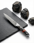 Couteau japonais petty en acier damas, lame fine gravée, manche résine noir et ambre, posé sur ardoise avec pierres volcaniques.
