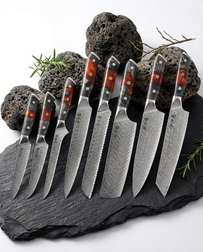 Set de 8 couteaux japonais en acier damassé avec manches noir et rouge, disposés sur ardoise noire avec pierres volcaniques et branches de romarin.