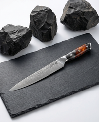 Couteau japonais sujihiki en acier damas, lame longue et fine, manche résine noir et ambre, présenté sur ardoise.