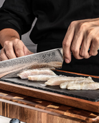 Couteau japonais Gyuto en acier damassé utilisé pour trancher un filet de poisson sur planche en bois.