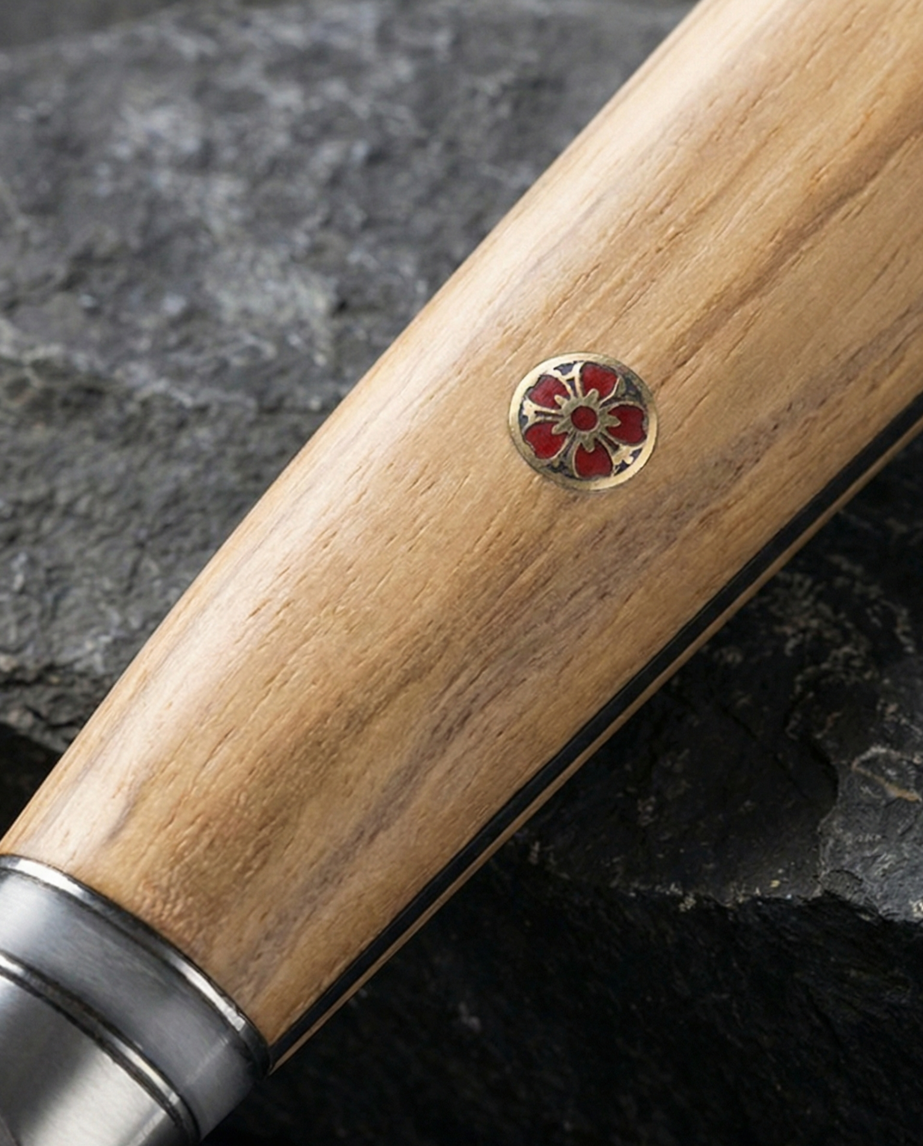Gros plan sur manche de couteau japonais en bois clair avec veinage naturel et insert décoratif rouge incrusté.