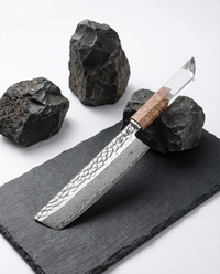 Couteau japonais en acier damassé à motif géométrique, manche en bois clair et résine transparente, posé sur ardoise noire avec pierres brutes