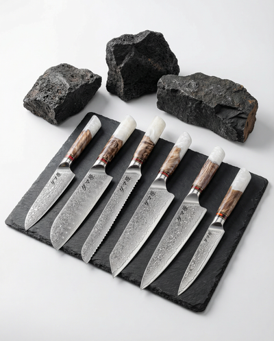 Set de 6 couteaux japonais damas avec manches bois et résine blanche, présentés sur ardoise noire et pierres brutes.