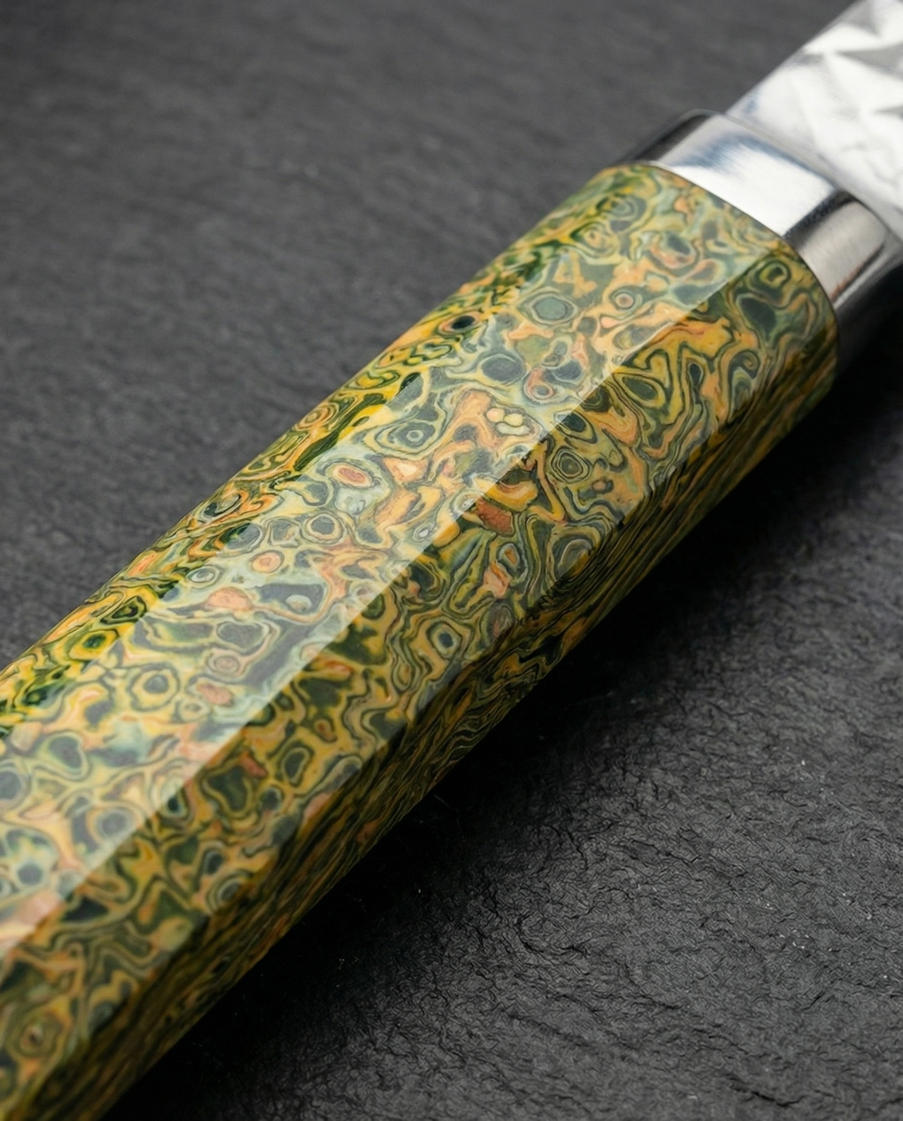 Gros plan sur le manche d’un couteau japonais Damas Origin en résine stabilisée vert jungle avec nuances jaune doré et motifs marbrés organiques, finition brillante sur fond ardoise noire.