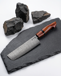 Couteau japonais nakiri en acier damas, manche ergonomique en bois rouge, présenté sur ardoise avec pierres noires.