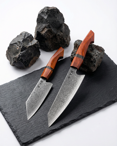 Set de 2 couteaux japonais damas, chef et santoku, manches bois rouge, présentés sur ardoise avec pierres brutes.