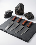 Set de 4 couteaux japonais en acier damas, manches bois rouge, présentés sur plaque en ardoise avec pierres brutes.