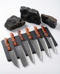 Set de 6 couteaux japonais en acier damas, manches bois rouge veinés, alignés sur ardoise noire avec pierres décoratives.
