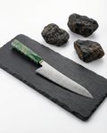 Couteau japonais kiritsuke en acier damas motif circulaire, manche vert marbré, lame longue posée sur ardoise noire.