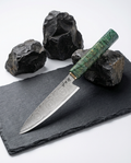 Couteau japonais chef en acier damas motif circulaire, manche vert marbré, présenté sur ardoise noire avec roches volcaniques.