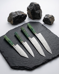 Set de 4 couteaux japonais en acier damas, manches verts texturés, présentés sur ardoise noire avec roches décoratives.