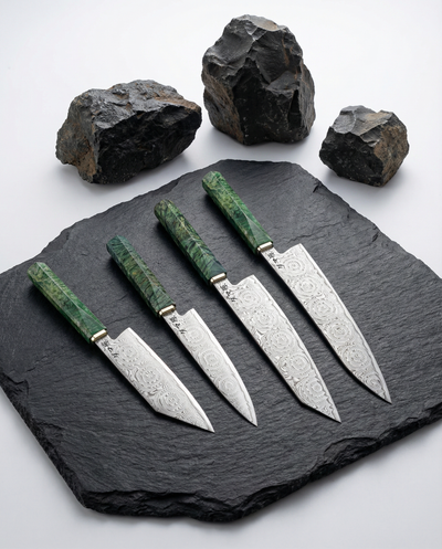 Set de 4 couteaux japonais en acier damas, manches verts texturés, présentés sur ardoise noire avec roches décoratives.