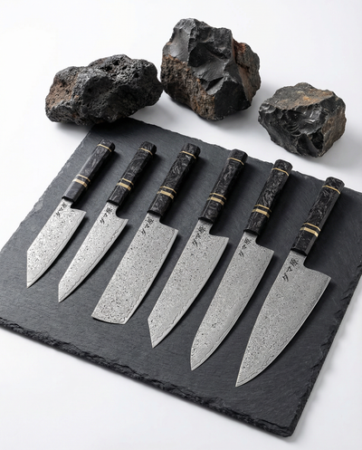 Set complet de 6 couteaux japonais en acier damas, manches noirs texturés avec anneaux dorés, présentés sur ardoise noire.