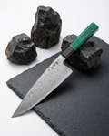 Couteau japonais en acier damassé avec manche vert texturé, posé sur ardoise noire entourée de pierres volcaniques