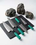 Set de 4 couteaux japonais en acier damassé avec manches verts texturés, posés sur ardoise avec pierres brutes