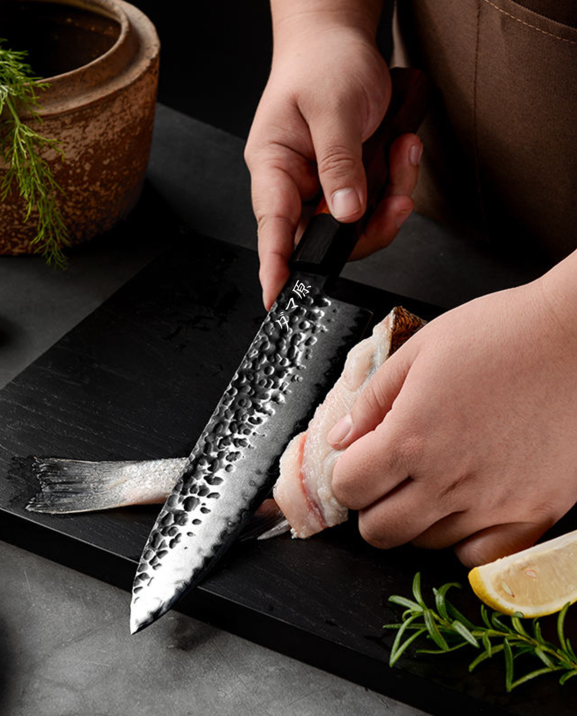 Couteau japonais en acier damassé martelé filet de poisson sur planche noire, mains tenant le manche, citron et herbes à côté