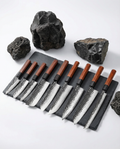 Set de neuf couteaux japonais en acier martelé, manches en bois foncé, alignés sur ardoise avec pierres brutes