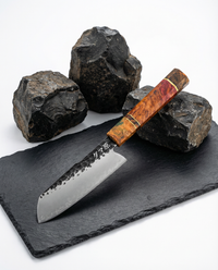 Couteau japonais en acier, manche en bois stabilisé rouge et ambre, posé sur ardoise noire avec pierres brutes