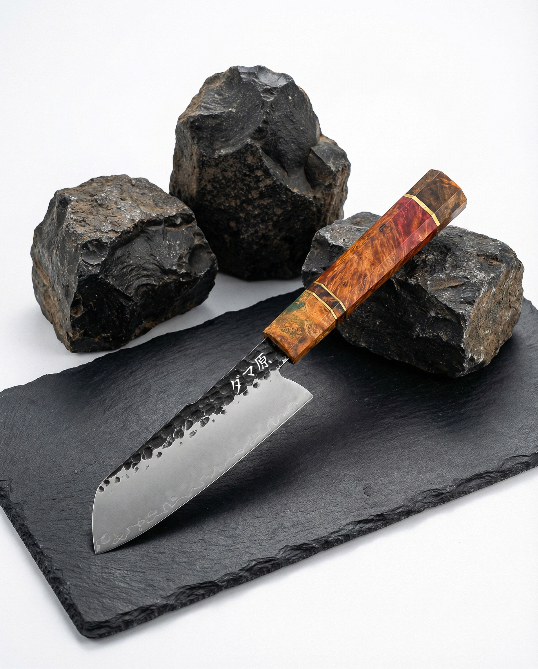 Couteau japonais en acier damassé martelé, manche en bois stabilisé rouge et ambre, posé sur ardoise noire avec pierres brutes