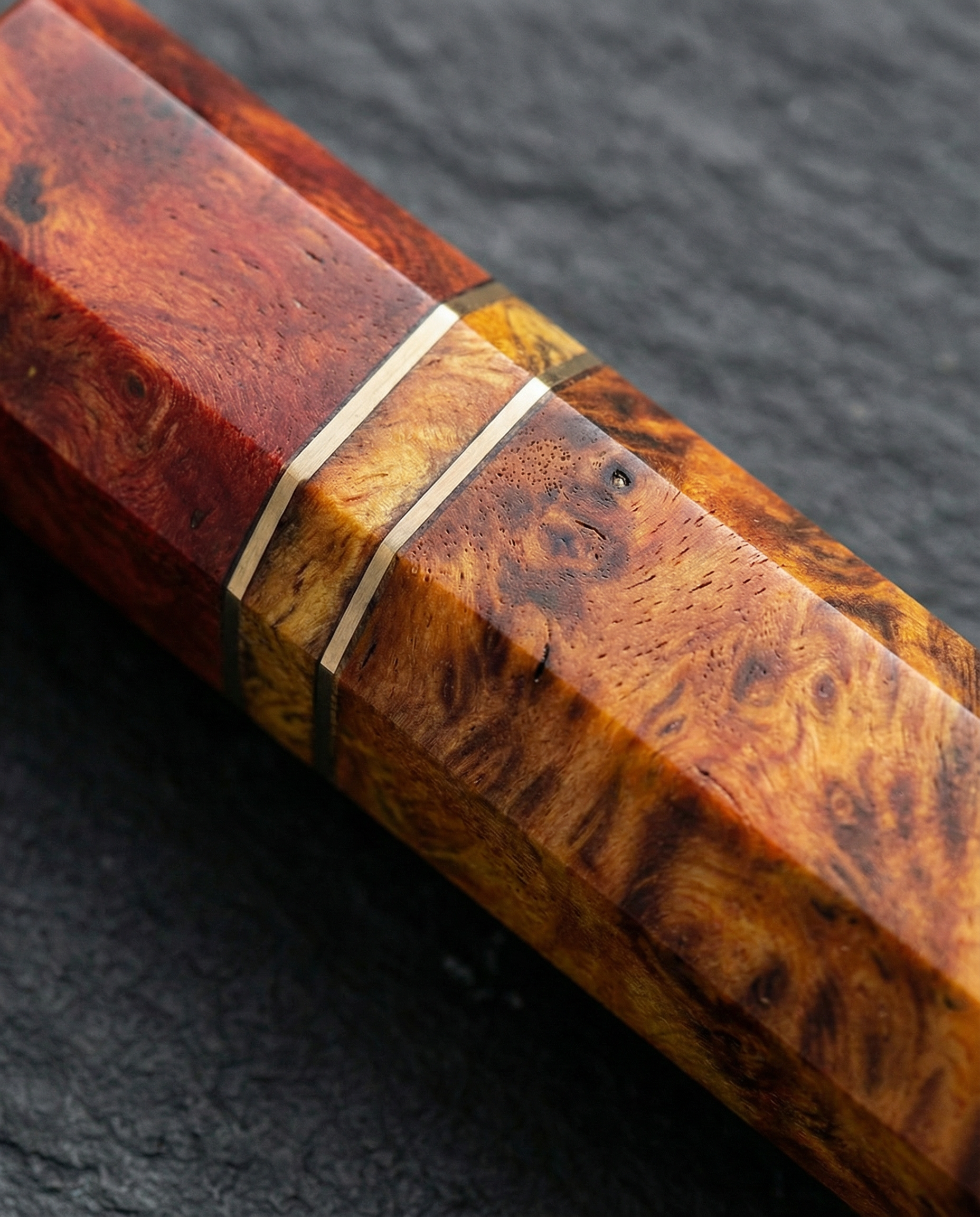 Gros plan sur manche de couteau japonais en bois stabilisé rouge et ambre, veinage marqué avec double liseré clair, posé sur ardoise noire