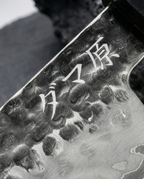 Gros plan sur couteau japonais en acier, lame gravée de caractères japonais, posé sur ardoise sombre
