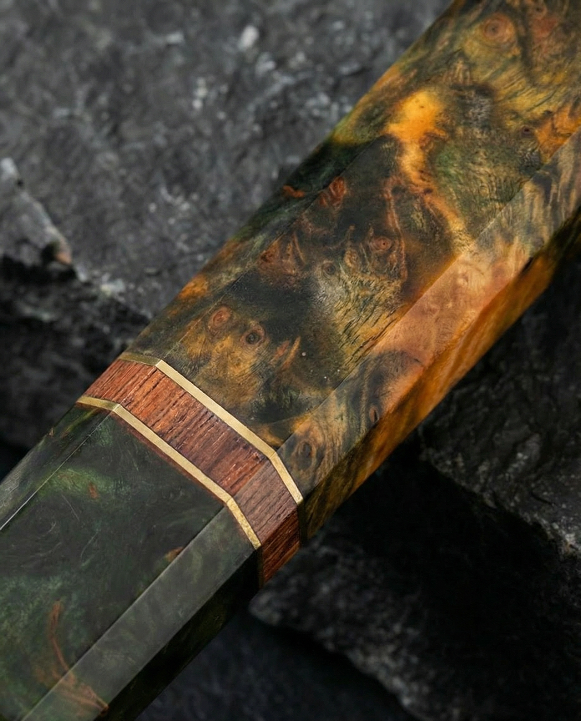 Gros plan sur manche de couteau japonais en bois stabilisé vert et ambre, veinage marqué avec insert en bois et liseré clair, posé sur pierre sombre