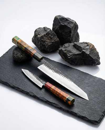Set de deux couteaux japonais en acier, manches en bois stabilisé coloré, posés sur ardoise avec pierres noires
