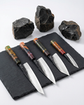 Set de cinq couteaux japonais en acier, manches colorés en bois stabilisé, posés sur ardoise avec pierres sombres