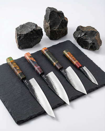 Set de cinq couteaux japonais en acier, manches colorés en bois stabilisé, posés sur ardoise avec pierres sombres
