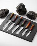 Set de six couteaux japonais en acier, manches colorés en bois, posés sur ardoise avec pierres volcaniques