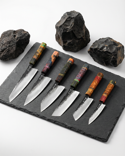Set de six couteaux japonais en acier, manches colorés en bois, posés sur ardoise avec pierres volcaniques