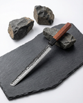 Couteau japonais en acier martelé à lame longue, manche en bois brun, posé sur ardoise noire avec pierres brutes