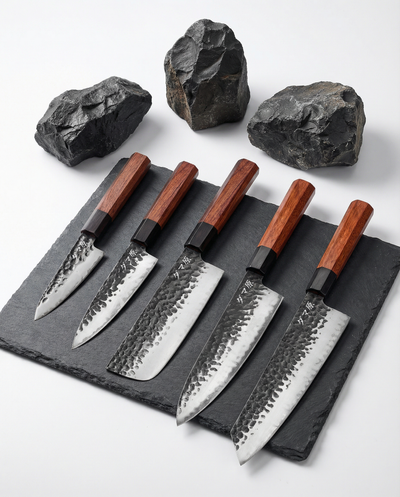 Set de cinq couteaux japonais en acier martelé, manches en bois brun, alignés sur ardoise avec pierres brutes
