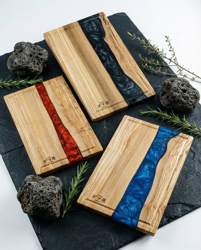 Trois planches en bois avec incrustations de résine rouge, bleue et noire, posées sur ardoise noire avec pierres volcaniques et branches de romarin